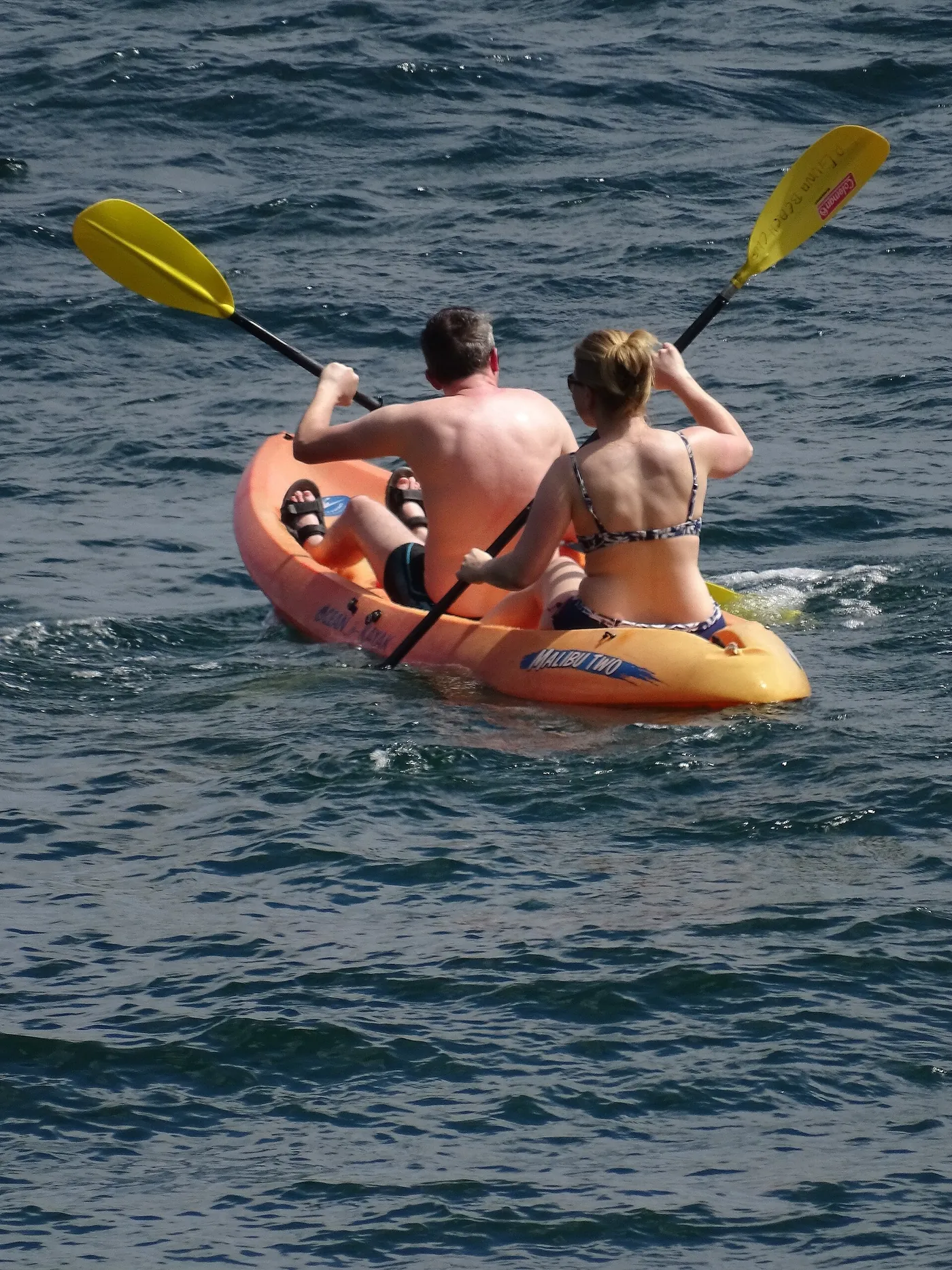 Two people paddling a kayak on calm blue water